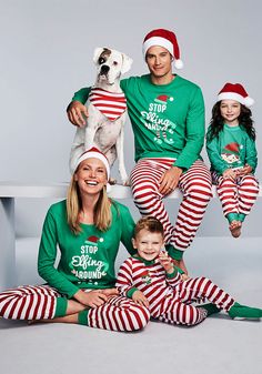 the family is wearing matching christmas pajamas and santa's helper hats as they pose with their dog