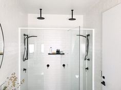 a walk in shower sitting next to a white tiled wall and floor with black fixtures