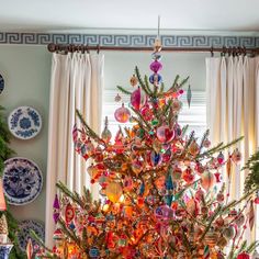 a brightly colored christmas tree in the corner of a room with plates on the wall