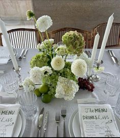 the table is set with white and green flowers, silverware, and menus