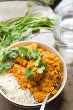 a bowl filled with rice and vegetables next to a glass of water on a table