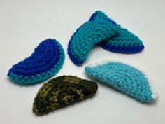 four crocheted objects are arranged on a white surface, one is blue and the other is green