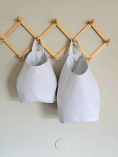 two white bags hanging on a wall with wooden pegs attached to the top and bottom