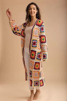 a woman wearing a colorful crochet cardigan standing in front of a beige background