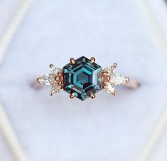 an emerald colored ring with three small white diamonds on the side and one blue diamond in the middle