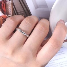 a woman's hand with a wedding ring on top of her finger next to an open book