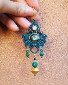 a person holding onto a blue and gold beaded pendant with beads on it's side