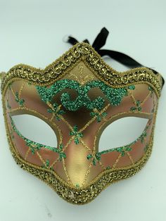 "This is a very nice original handmade and hand painted Venezia masquerade face mask made in Italy. The design on the shiny gold and orange face mask features turquoise blue and multi-color glitter with a border of gold lace and gold rope around the edges. It comes with a black ribbon tie and is stamped on the back \"Original Hand Painted Made in Italy Venezia\". The mask measures approximately 6 5/8\" long and 3 3/4\" wide and is in very good preowned condition with light wear on the back of th Fantasy Masks For Carnival And Festivals, Fantasy Carnival Mask For Festivals, Green Carnival Masks And Prosthetics, Green Masks For Carnival Costume Party, Halloween Eye Mask As A Gift, Halloween Eye Mask Gift, Green Masquerade Mask For Mardi Gras, Green Mask For Masquerade Carnival, Green Masks For Masquerade Carnival