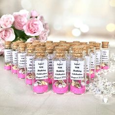 small bottles filled with pink and gold confetti sitting on a table next to flowers