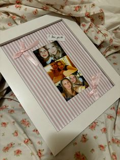 a white frame with pink ribbon around it and photos on the inside, in front of a flowered bed sheet