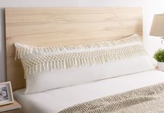 a bed with white linens and pillows on it, next to a small potted plant