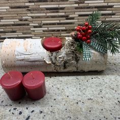 two red candles sitting on top of a piece of wood next to a christmas decoration