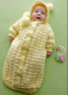 a baby wearing a yellow crochet sleeping bag next to a toy on a green surface