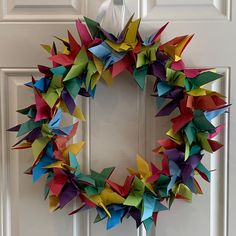 a wreath made out of colorful origami paper hanging on a white door frame