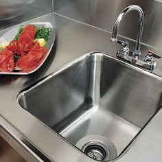 a stainless steel kitchen sink next to a plate with lobsters and lettuce