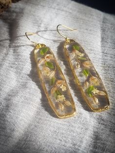 These elegant pressed flower earrings, with their delicate baguette silhouette, feature hand-picked dried white bell flowers meticulously preserved in resin . A perfect statement for those who appreciate understated style and the enduring charm of nature. 🌿 Hypoallergenic gold-filled earrings hooks, a reliable choice, particularly for those with sensitive skin. 🌿 Every natural element featured in my jewelry is carefully sourced by me locally and preserved using a technique that maintains their Cheap Pressed Flowers Earrings, Elegant White Earrings With Pressed Flowers, Elegant Clear Jewelry With Pressed Flowers, Elegant Pressed Flowers Jewelry For Everyday, Elegant Floral Print Drop Earrings, Elegant Flower Earrings With Floral Print For Gift, Elegant Floral Print Flower Earrings For Gift, Elegant Floral Print Flower Earrings As Gift, Elegant Resin Earrings With Pressed Flowers