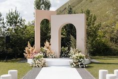 an outdoor ceremony setup with white flowers and candles on the ground in front of it