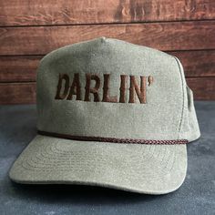 Vintage Style Darlin' Embroidered Faded Canvas Snapback Trucker Rope Hat with Free Shipping. White stitched text/logo. Condition is "New with tags". Shipped with USPS First Class. Step into the world of the great outdoors with our Darlin' Stitched Faded Canvas Rope Hat. With its faded canvas and rope accents, this hat exudes rustic charm and pays tribute to the iconic country music legends. Plus, enjoy free shipping on this vintage-inspired accessory that's perfect for any country music enthusia Vintage Adjustable Baseball Cap With Embroidered Logo, Vintage Curved Brim Hat With Letter Embroidery, Vintage Curved Bill Hat With Embroidered Logo, Vintage Adjustable Hat With Letter Embroidery, Retro Adjustable Trucker Hat With Embroidered Logo, Vintage Adjustable Hats With Embroidered Logo, Vintage Adjustable Snapback Hat With Embroidered Logo, Embroidered Trucker Hats, Western Wear Outfits