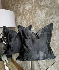 two black velvet pillows sitting on top of a table next to a lamp and mirror