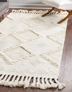 a white rug with tassels on top of it in front of a chair