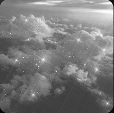 black and white photograph of clouds with stars in the sky at night, taken from an airplane window