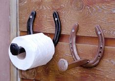 a pair of horseshoes hanging on the side of a wooden wall next to a roll of toilet paper