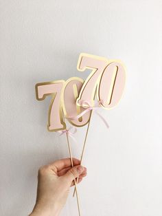 a person holding up a pink and gold 70th birthday cake topper on a stick