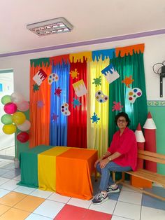 a woman is sitting on a bench in front of colorful curtains and decorations at a birthday party