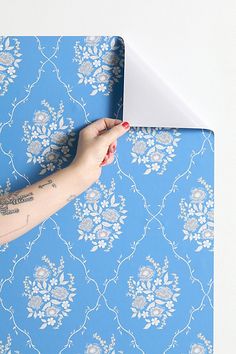 a woman's arm with tattoos on it and a blue floral wallpaper