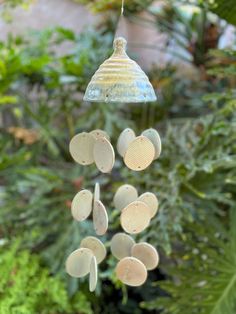 a wind chime hanging from a tree in a garden with lots of green plants