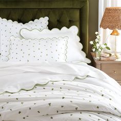 a bed with white sheets and green headboard next to a lamp on a nightstand