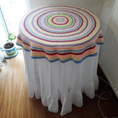 a white table with a multicolored quilt on it's top and wooden floor