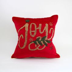 a red christmas pillow with the word joy on it and gold sequins is sitting in front of a white background