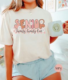 a woman holding a mug and smiling while wearing a t - shirt with the word senior on it