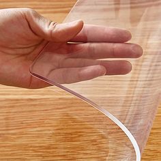 a person holding their hand out over a piece of clear plastic on top of a wooden table