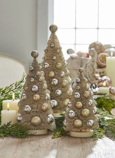 two small christmas trees sitting on top of a table next to candles and greenery