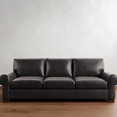 a black leather couch sitting on top of a hard wood floor next to a white wall