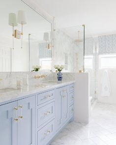 a bathroom with marble counter tops and blue cabinetry, along with gold pulls on the doors