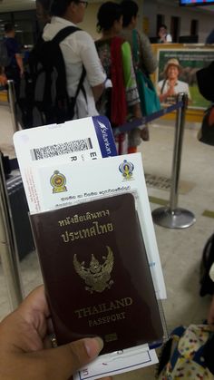 a person holding up a thai passport in front of other people at an airport terminal