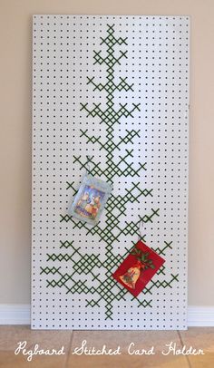 a cross stitch christmas tree is hanging on the wall next to a card holder with pictures