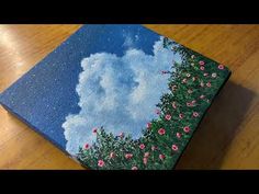 a painting on a wooden table with clouds in the sky and flowers growing out of it