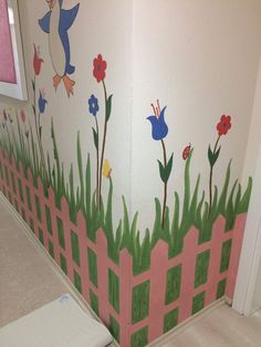 a painted mural on the side of a wall with flowers and birds in grass, behind a pink fence