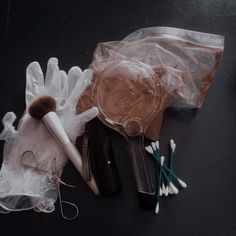 an assortment of makeup products in plastic bags on a black surface with one brush and two pairs of scissors