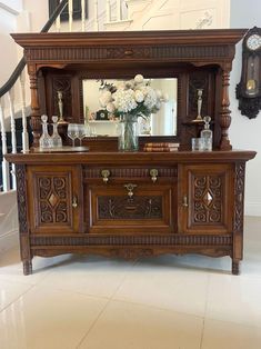 an ornate wooden dresser with flowers and vases in front of the mirror on the wall