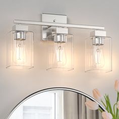 three light bathroom fixture with clear glass shades on the wall and round mirror above it