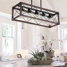 a light fixture hanging over a kitchen table with potted plants and flowers on it