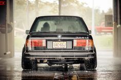 the back end of a car parked in a parking lot on a rainy day,