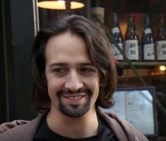 a man with long hair and beard smiling at the camera in front of a store