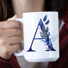 a woman is holding a coffee mug with the letter a on it and leaves painted on it