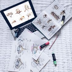 an open laptop computer sitting on top of a bed next to papers and markers with drawings